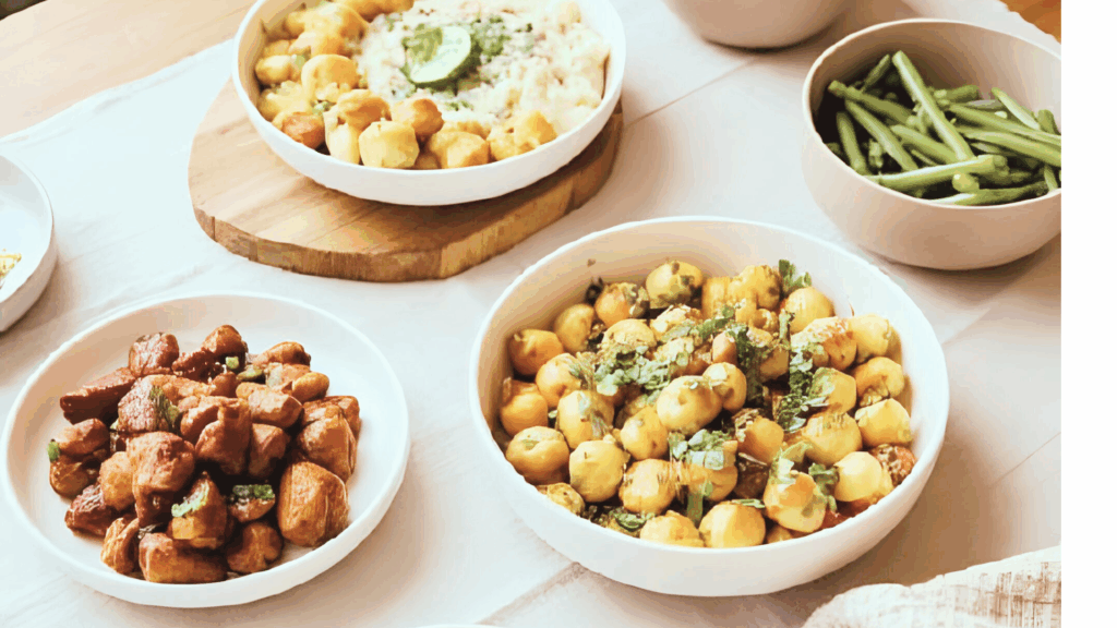 "Overhead view of a beautifully styled Thanksgiving table featuring roasted carrots, sweet potatoes, Brussels sprouts, wild rice, and green beans in neutral ceramic bowls, set on a warm linen tablecloth."